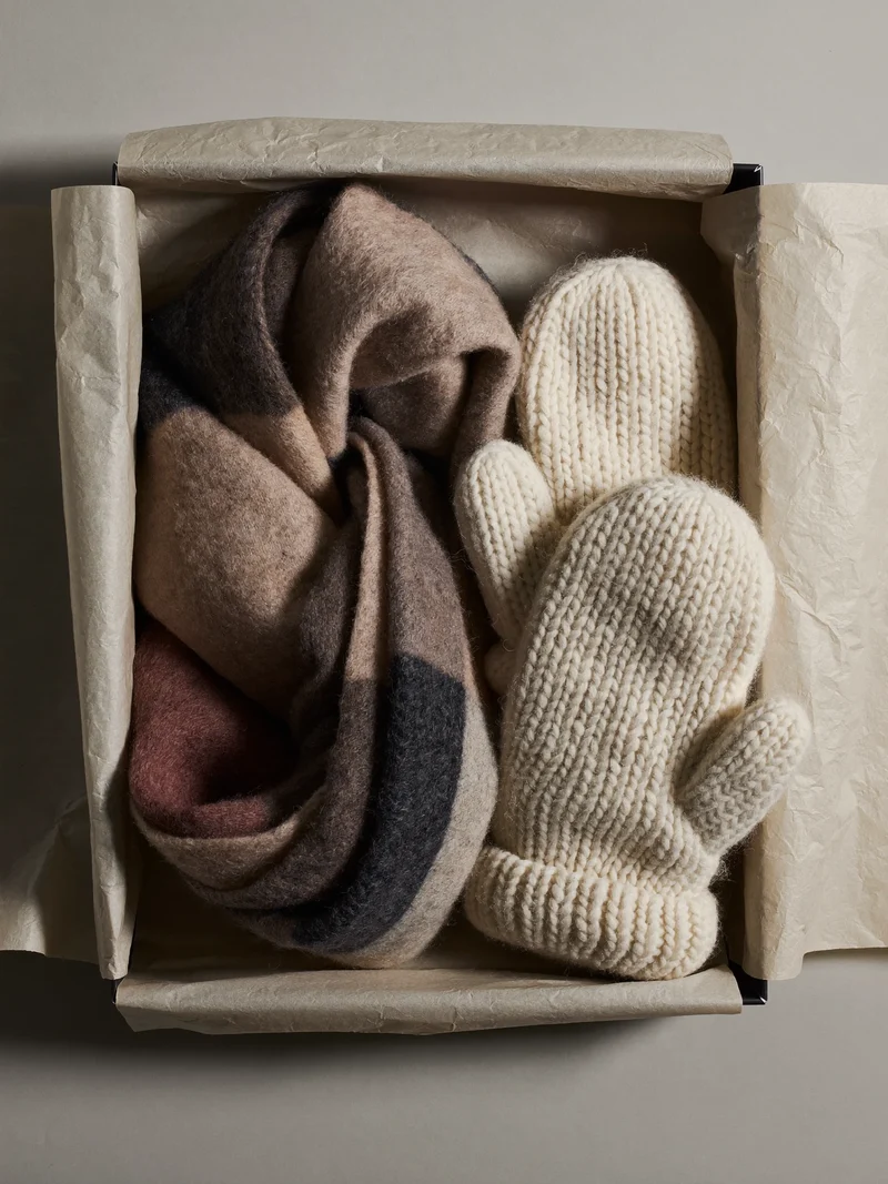 Wollschal und Strickhandschuhe in offener Geschenkbox mit Seidenpapier, illustrativ